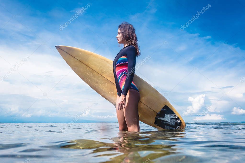 side view of attractive sportswoman in wetsuit with surfing board standing in ocean at Nusa dua Beach, Bali, Indonesia