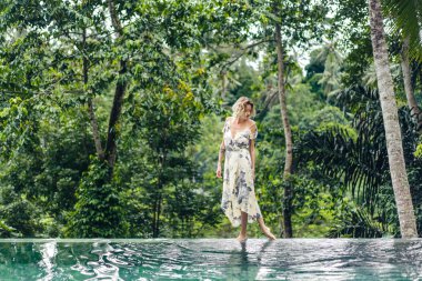 içinde yeşil bitkiler ile yüzme havuzu yakındaki arka planda, ubud, bali, Endonezya yürüme çekici sarışın kadın