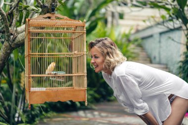 side view of smiling woman looking at bird in cage, ubud, bali, indonesia