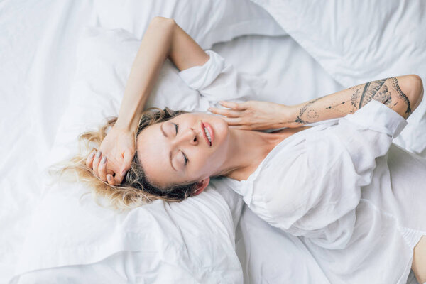 beautiful blond woman with eyes closed in white shirt resting on bed