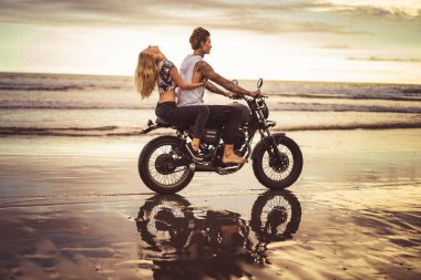 side view of girlfriend hugging boyfriend from back on motorcycle on ocean beach  clipart