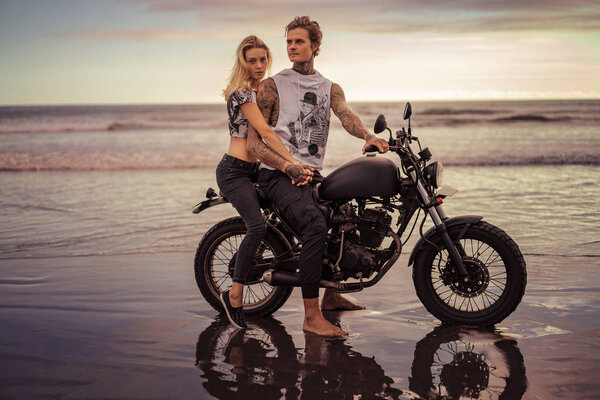 couple holding hands and sitting on motorcycle on ocean beach 