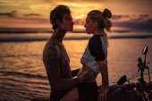 leidenschaftliches Paar umarmt sich bei Sonnenuntergang auf dem Motorrad am Strand