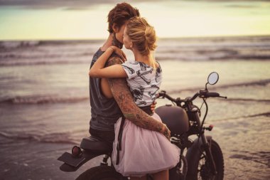 passionate couple hugging on motorcycle on ocean beach during beautiful sunrise  clipart