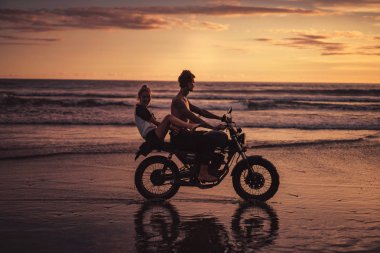 eğleniyor ve okyanus plaj üzerinde motosiklet Binme bir çift yan görünüm 