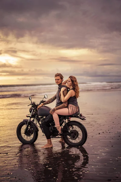 彼氏と日の出の間にビーチでのバイクに座って彼女の側面図  — 無料ストックフォト