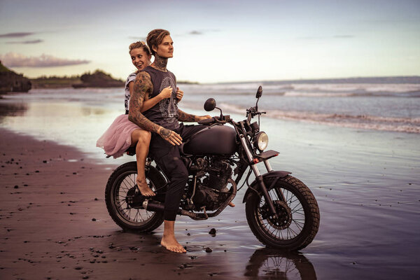 smiling girlfriend hugging boyfriend on motorcycle on ocean beach