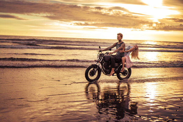 affectionate boyfriend and girlfriend riding motorcycle on ocean beach during sunrise