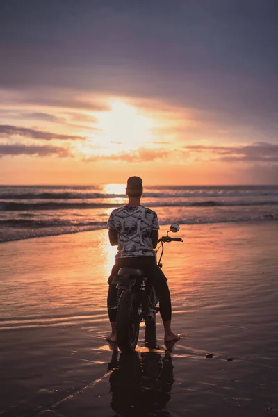 后面的人坐在摩托车上的海洋海滩和看美丽的日落 — 免费的图库照片