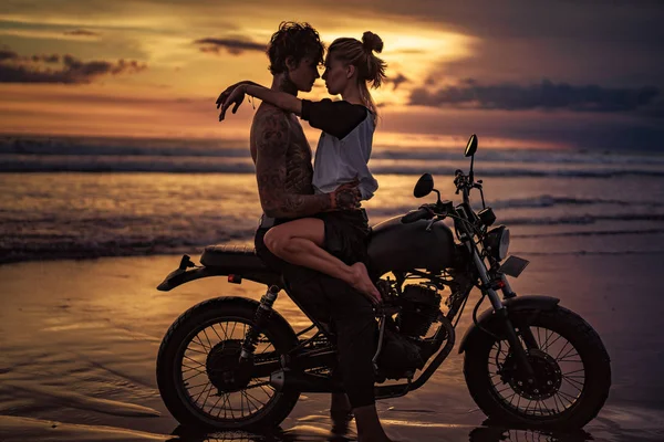夕阳西下时 一对热情的情侣骑摩托车在沙滩上拥抱 — 图库照片