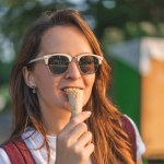 Smiling young woman in sunglasses eating ice cream