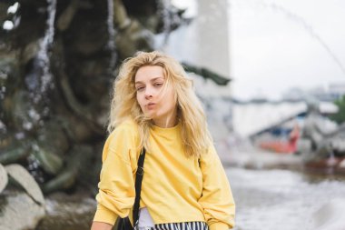 selective focus of young attractive woman looking at camera in front of fountain  clipart