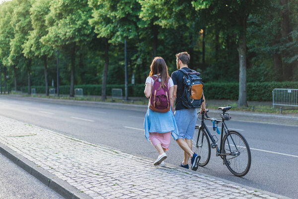 rear view of couple with backpacks and bicycle walking at street