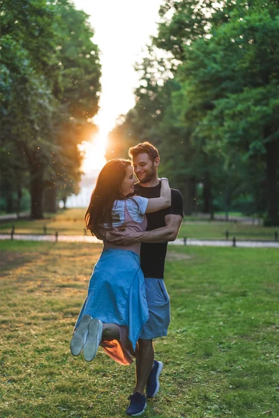 Sorridente Homem Segurando Jovem Namorada Parque Durante Pôr Sol — Fotografia de Stock