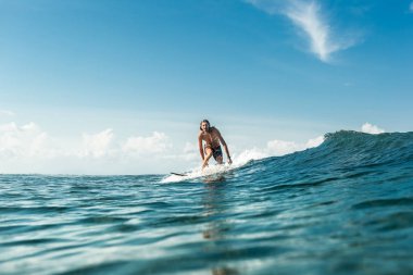 Nusa Dua Beach, Bali, Endonezya, okyanusta dalgaları sürme yakışıklı erkek sörfçü uzak görünümünü