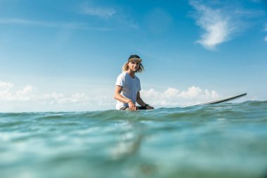 Okyanusu Nusa Dua Beach, Bali, Endonezya sörf tahtası üzerinde oturan genç erkek sörfçü seçici odak