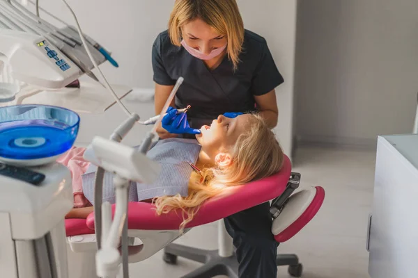 dentist in latex gloves and medical mask treating little kids teeth at dentist office