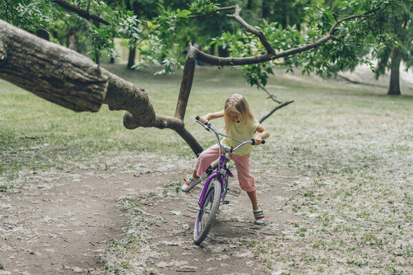 kid with bicycle standing near tree branch in park