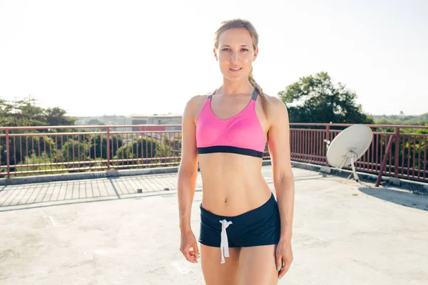 Lächelnde junge Sportlerin, die auf dem Dach steht und in die Kamera schaut — Stockfoto