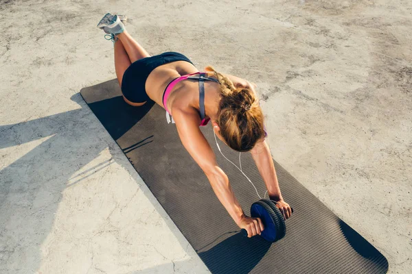 Visão de alto ângulo de esportista em fones de ouvido fazendo exercício com rolo abs no tapete de fitness — Fotografia de Stock