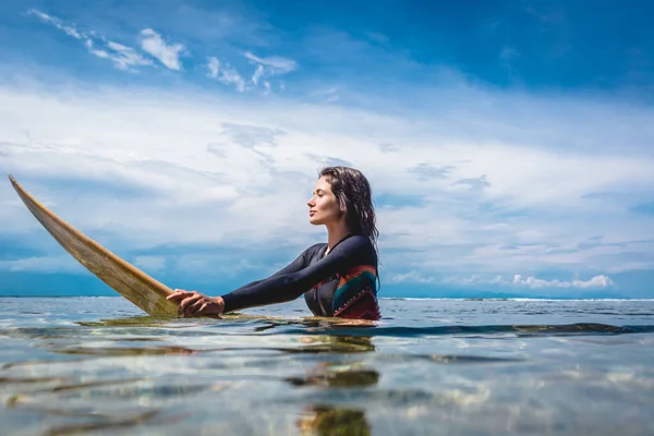 Вид сбоку молодой женщины в гидрокостюме на доске для серфинга в океане на пляже Нуса-дуа, Бали, Индонезия — стоковое фото
