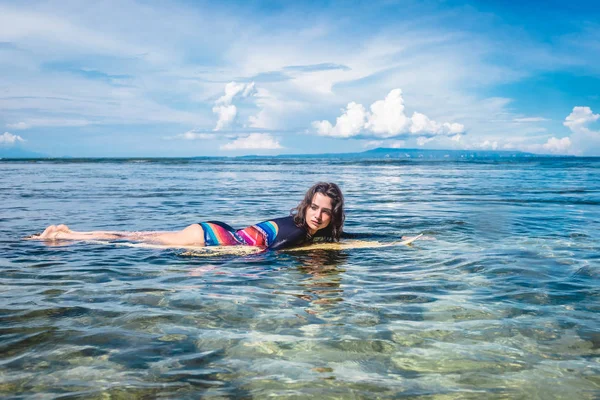 Вид сбоку молодой женщины в гидрокостюме на доске для серфинга в океане на пляже Нуса-дуа, Бали, Индонезия — стоковое фото