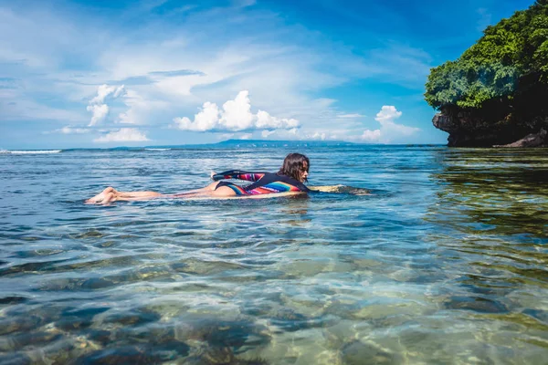 Side view of young sportswoman in wetsuit on surfing board in ocean at Nusa dua Beach, Bali, Indonesia — Stock Photo