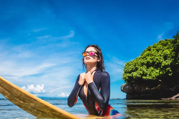 Спортсменка в гидрокостюме и солнцезащитных очках на доске для серфинга в океане на пляже Нуса Дуа, Бали, Индонезия — стоковое фото