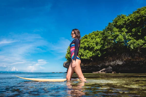 Attraktive junge Frau im Neoprenanzug mit Surfbrett posiert im Meer am Strand von Nusa Dua, Bali, Indonesien — Stockfoto