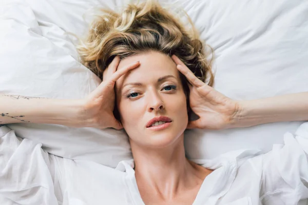 Overhead view of beautiful blond woman in white shirt resting on bed — Stock Photo