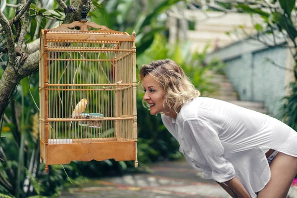 Vue latérale d'une femme souriante regardant un oiseau en cage, ubud, bali, indonesia — Photo de stock
