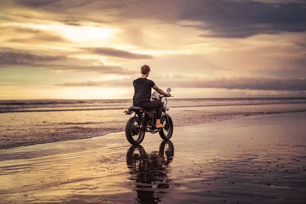 Back view of tattooed biker riding motorbike on ocean beach — Stock Photo