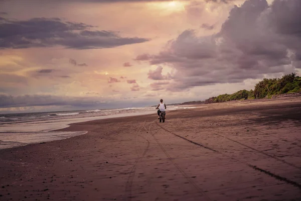 Vista trasera del hombre a caballo motocicleta en la playa del océano — Stock Photo