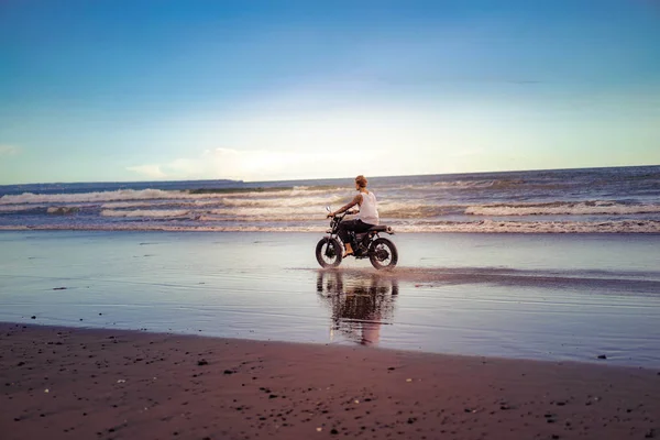Tattooed man riding motorcycle on ocean beach during sunrise — Stock Photo