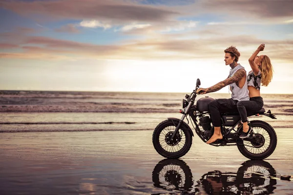 Side view of couple riding motorcycle on ocean beach — Stock Photo