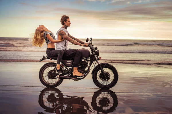 Side view of young couple riding motorcycle on ocean beach — Stock Photo