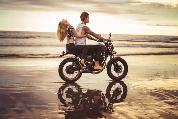 Vista lateral da namorada abraçando namorado de volta na motocicleta na praia do oceano — Fotografia de Stock