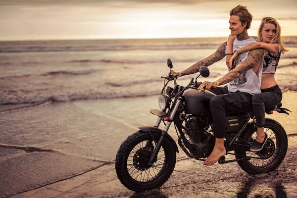 Leidenschaftliches Paar fährt Motorrad am Strand des Ozeans bei Sonnenaufgang — Stockfoto