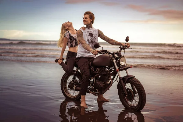 Novia tocando novio y sentado en motocicleta en la playa del océano - foto de stock