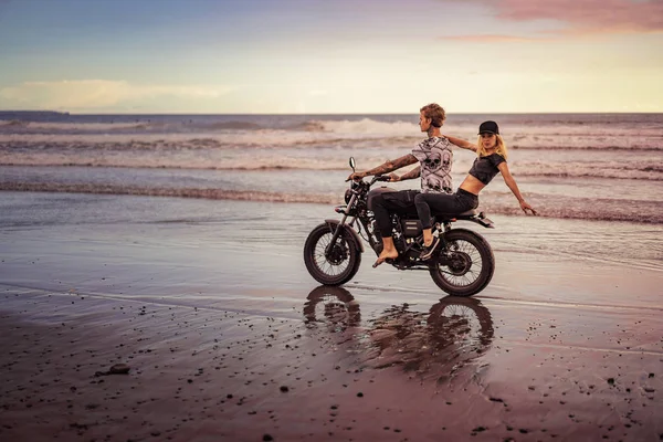 Young couple riding motorcycle on ocean beach — Stock Photo