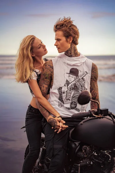 Couple holding hands and looking at each other near motorcycle on ocean beach — Stock Photo