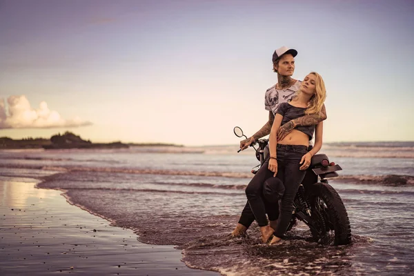 Novio con estilo abrazo novia cerca de la motocicleta en la playa del océano - foto de stock