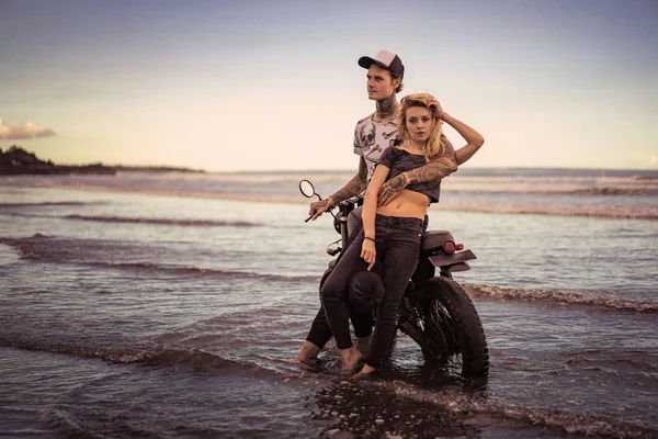 Coppia elegante in piedi vicino moto sulla spiaggia dell'oceano — Foto stock