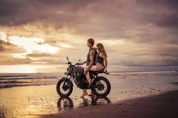 Хлопець і дівчина обіймаються на мотоциклі на пляжі під час сходу сонця — стокове фото