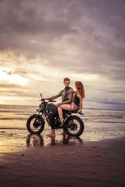 Boyfriend and girlfriend sitting on motorcycle at sandy beach — Stock Photo