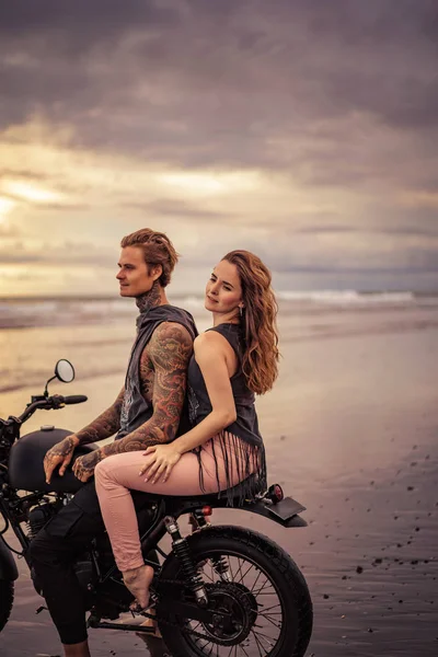 Novia apasionada y novio sentado en motocicleta en la playa durante el amanecer - foto de stock