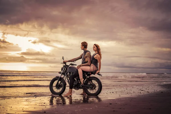 Лагідна пара сидить на мотоциклі на пляжі під час сходу сонця — стокове фото