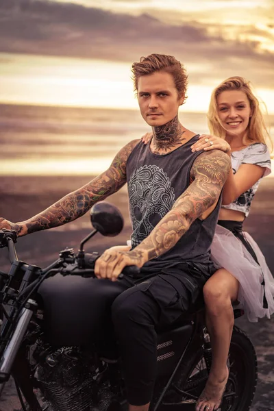 Young heterosexual couple sitting on motorcycle and looking at camera at beach — Stock Photo