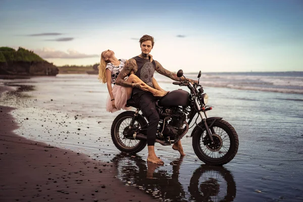 Casal apaixonado abraçando na moto na praia do oceano durante o belo nascer do sol — Fotografia de Stock