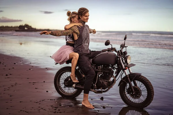 Бойфренд, сидящий на мотоцикле с распростертыми объятиями на берегу океана — стоковое фото